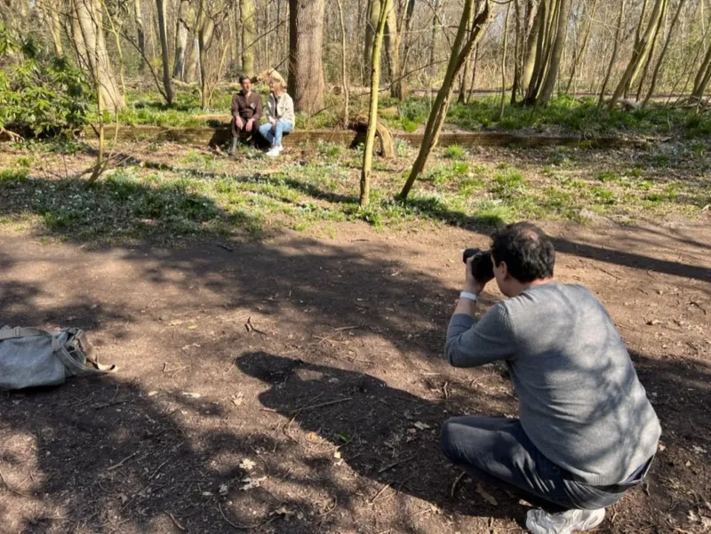 Fotograaf hurkt om een gezin op een bankje te fotograferen in een zonnig bos