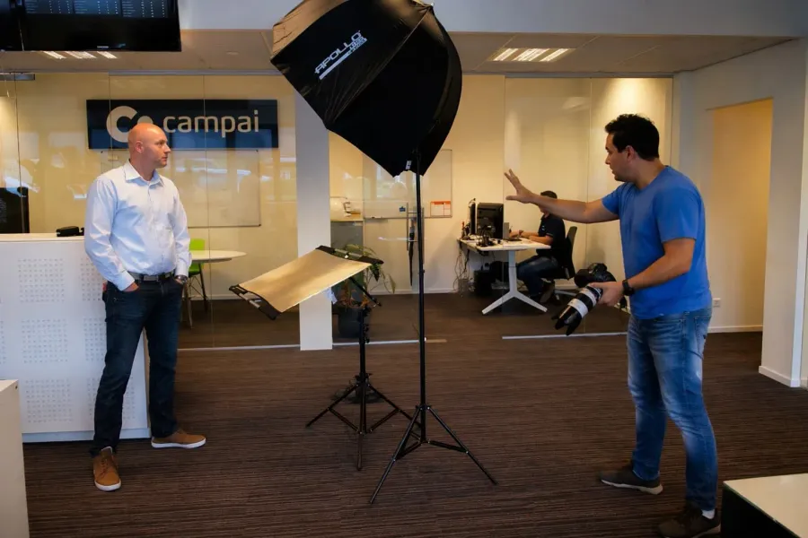 Fotograaf maakt foto van man in kantoor met studio verlichting en reflectiescherm.