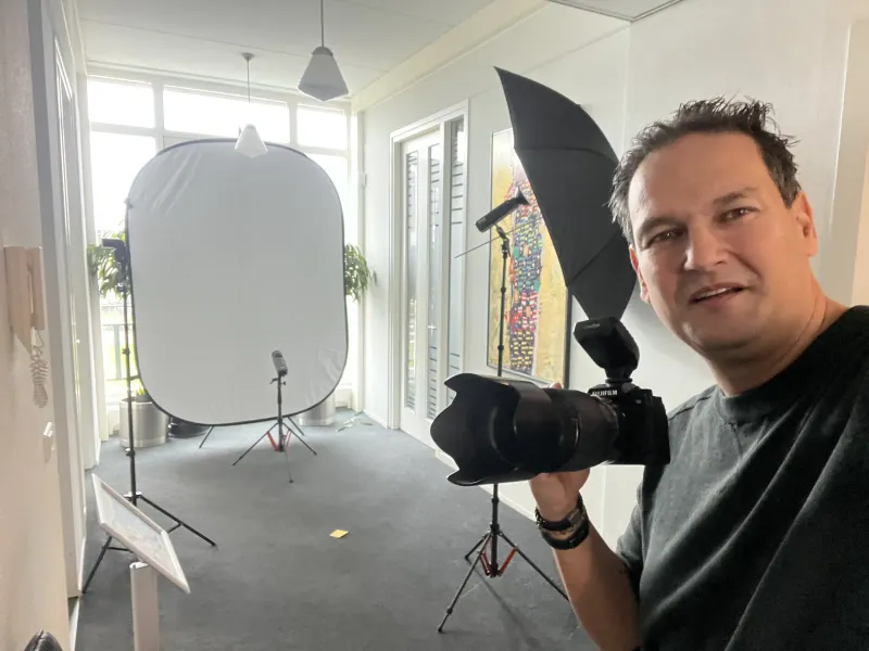 Fotograaf met camera naast een opvouwbare achtergrond en een kledingrek in een lichte ruimte