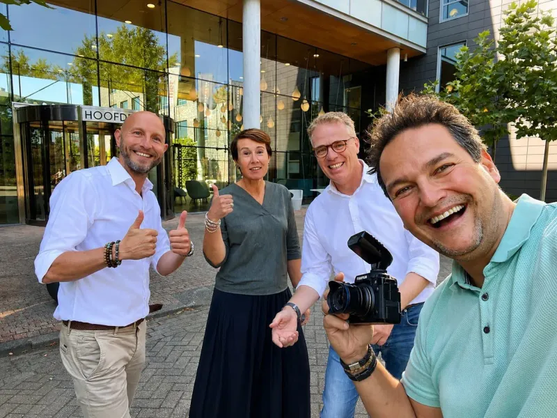 Fotograaf maakt buiten een kantoorpand een selfie met vier mensen die duimen opsteken