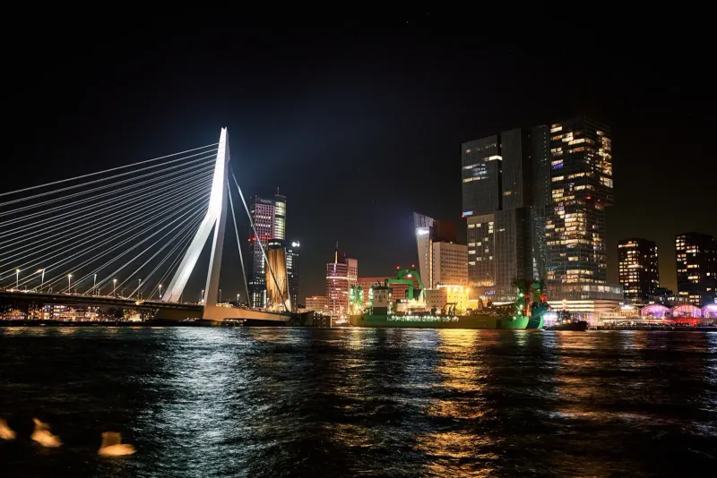 De verlichte Erasmusbrug en de skyline weerspiegeld in de Maas tijdens het blauwe uur