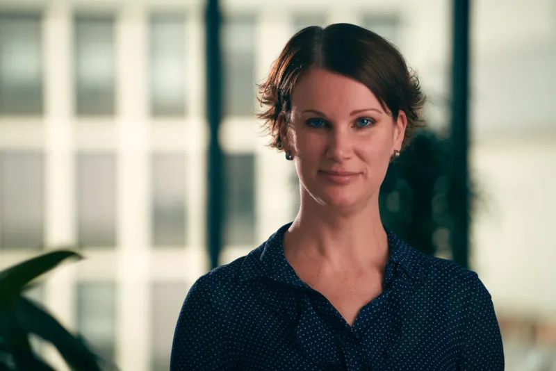 Zakelijk portret van een vrouw in een donkere blouse voor een kantoorraam met planten
