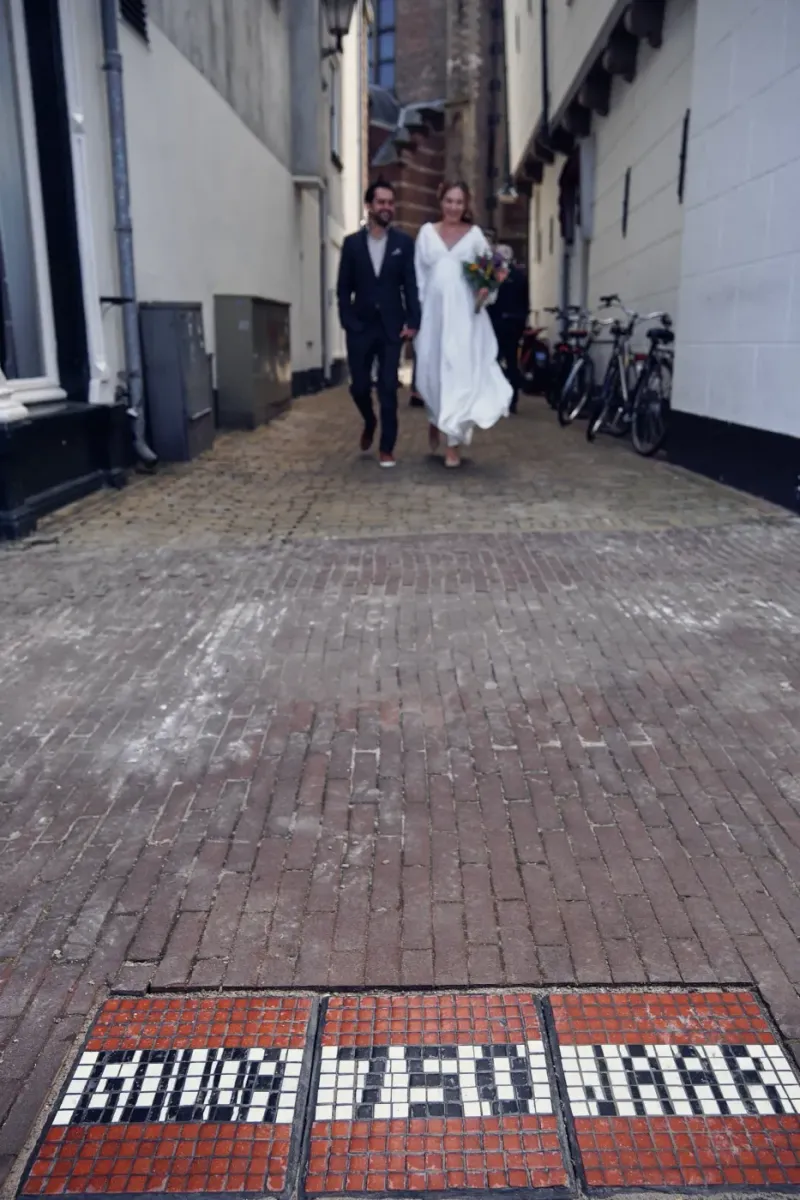 Bruidspaar loopt door een smalle steeg met een tegelmozaïek in de bestrating