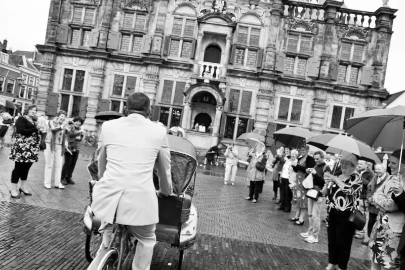 Zwart-witstraatbeeld van een man op een bakfiets voor het renaissancestadhuis met een groep toeristen