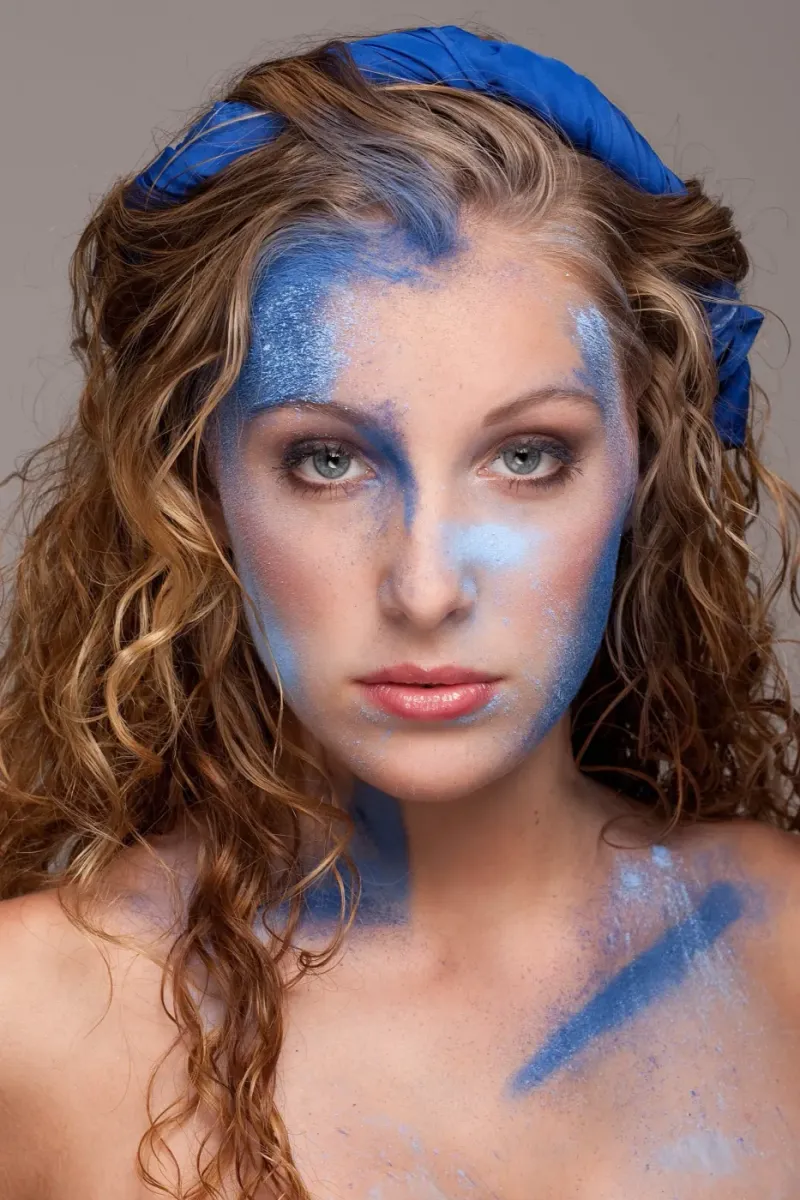 Creatief beautyportret van een vrouw met blauwe schmink en blauwe stof in het haar