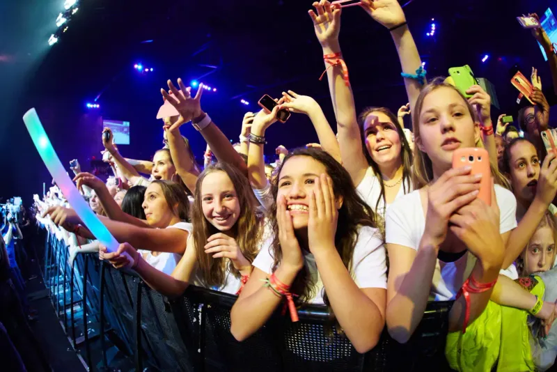 Juichend jong publiek met glowsticks aan de barrier tijdens een concert