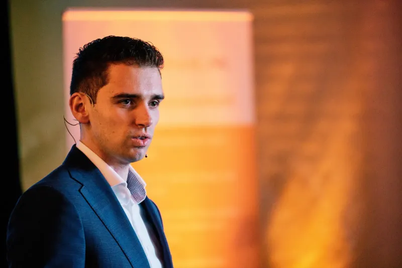 Zakelijk portret van een jonge man in een blauw colbert tegen een warme oranje achtergrond