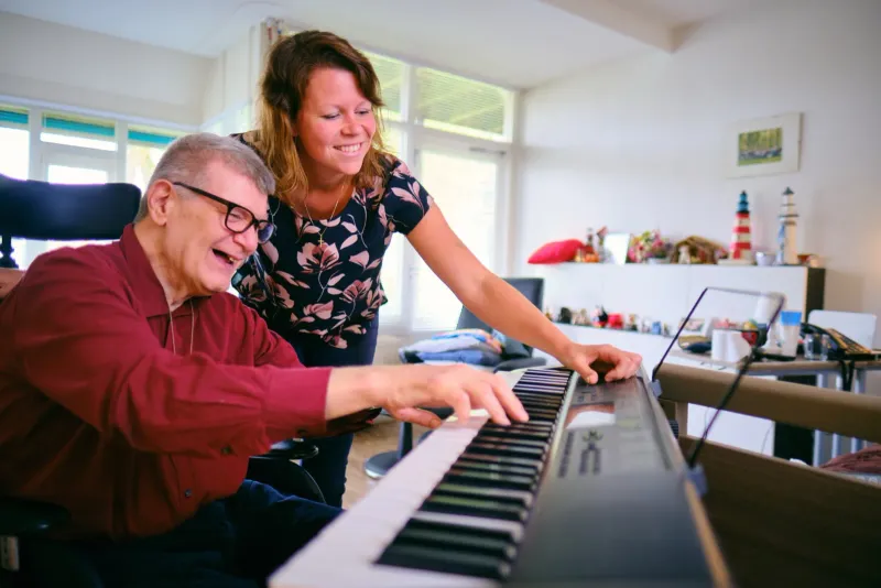 Man speelt keyboard terwijl een vrouw meekijkt en meespeelt in een lichte woonkamer