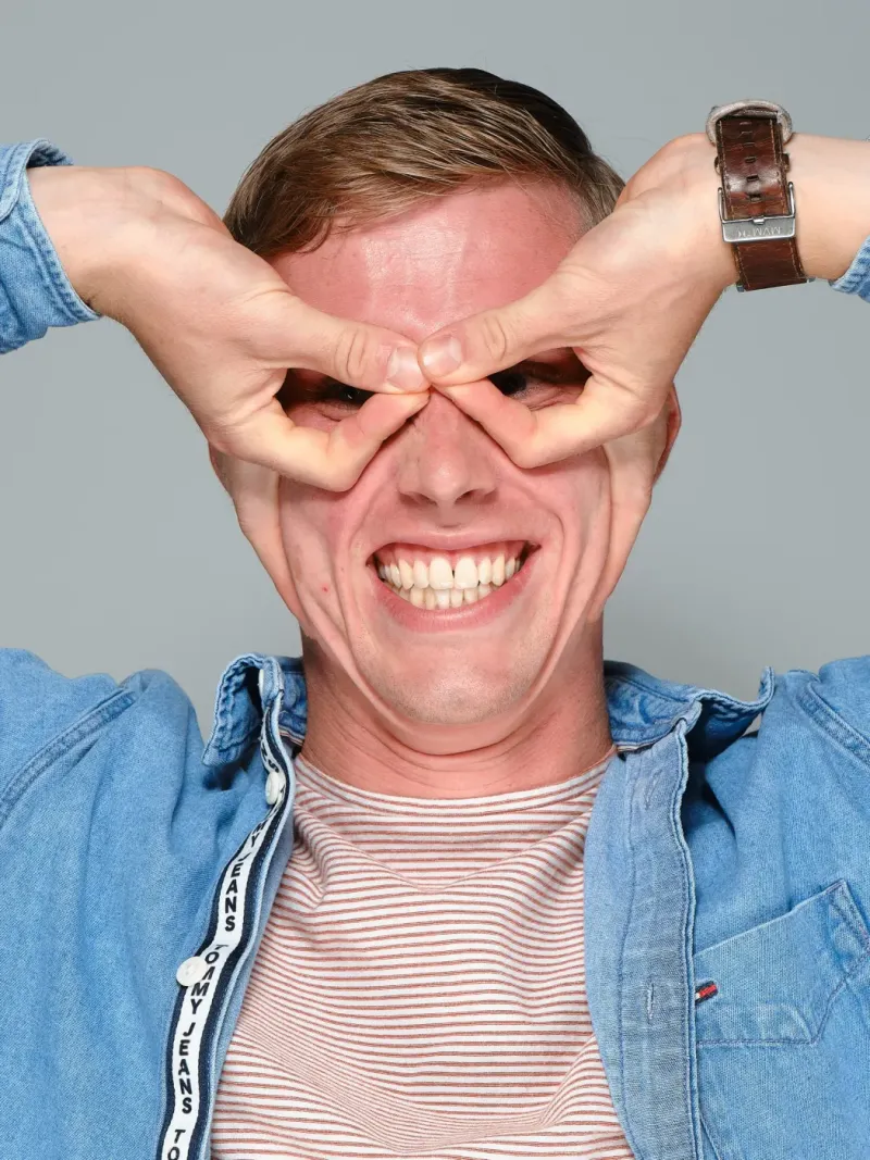 Speels portret van een lachende man die met zijn handen een bril om zijn ogen vormt