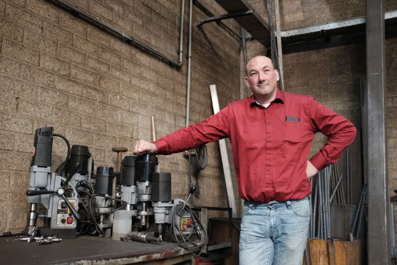 Man in een rood werkhemd leunt op booropstellingen in een werkplaats