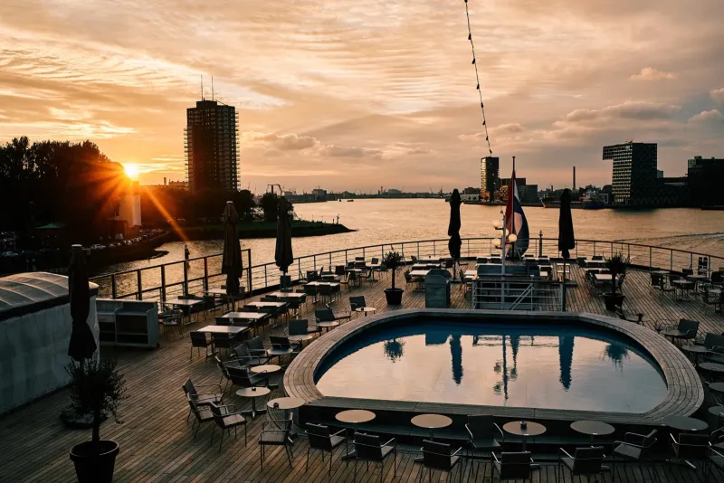 Dakterras met een gebogen zwembad bij zonsondergang en de haven op de achtergrond