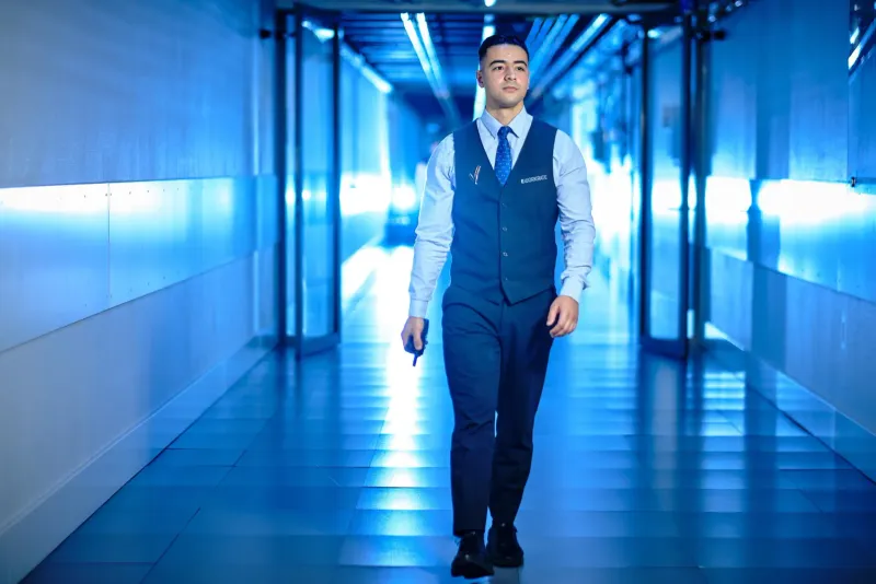 Man in gilet en stropdas loopt door een gang die baadt in blauw licht