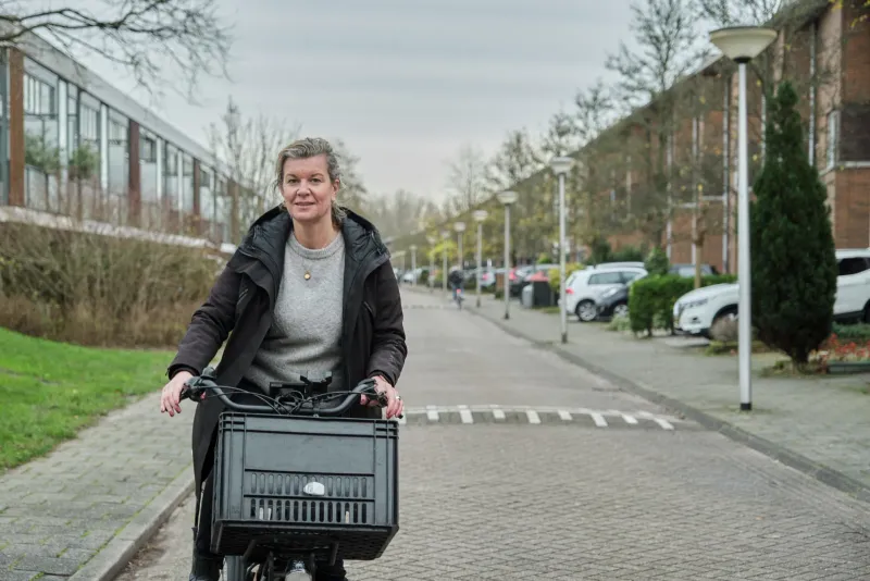 Vrouw fietst door een straat langs een oud fabriekspand naar de camera toe
