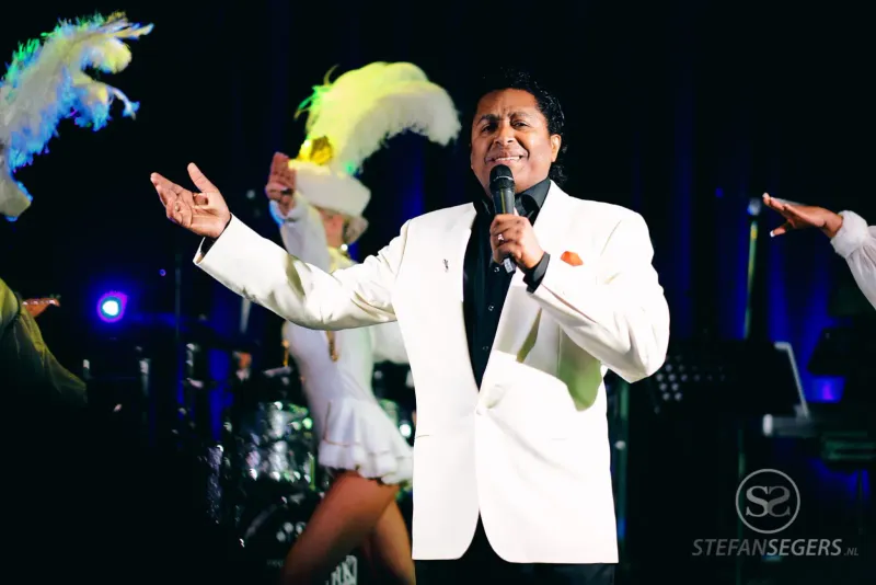 Entertainer in wit pak met microfoon en showgirls met verentooien op een podium