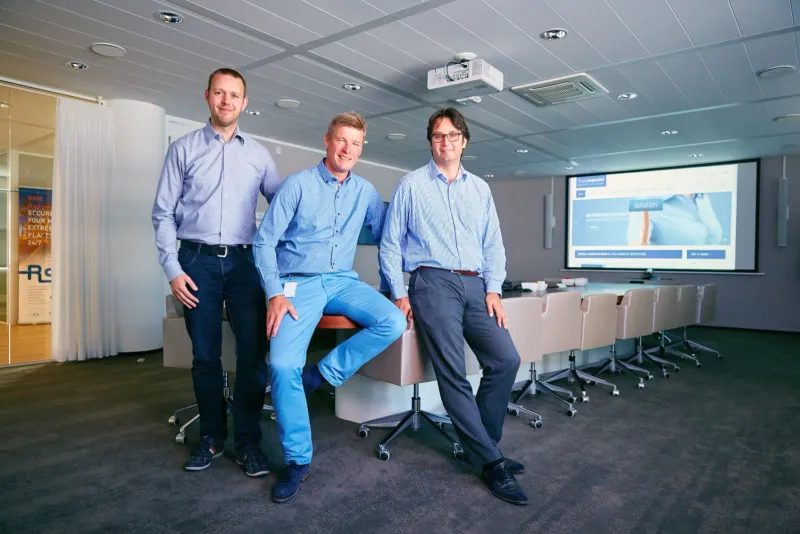 Drie mannen in zakelijke kleding in een moderne vergaderzaal met presentatiescherm