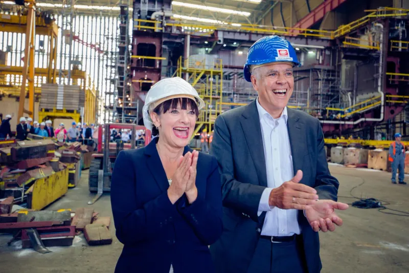Twee mensen met bouwhelmen applaudisseren lachend in een scheepswerf