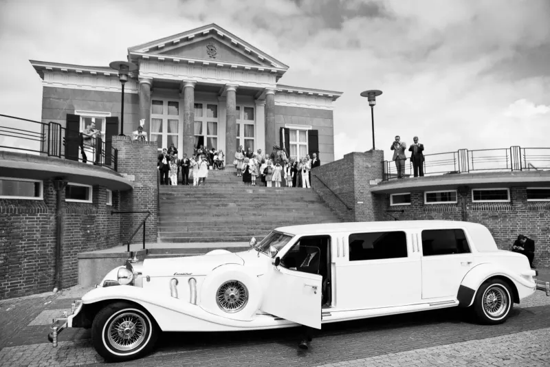 Witte stretchlimousine voor een klassiek gebouw met bruiloftsgasten op de trap