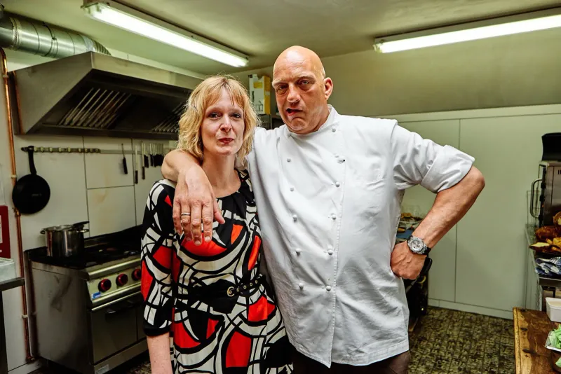Vrouw met haar arm om een kok in koksbuis in een professionele keuken