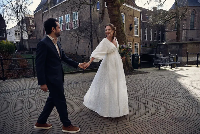 Bruidegom leidt de bruid aan de hand over een plein met historische gebouwen