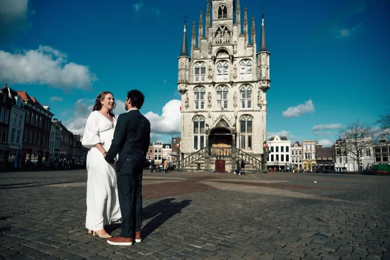 Bruidspaar omhelst elkaar op de Markt voor het gotische stadhuis van Gouda