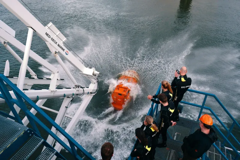Oranje snelle reddingsboot raakt het water naast een opleidingsschip, van bovenaf gezien
