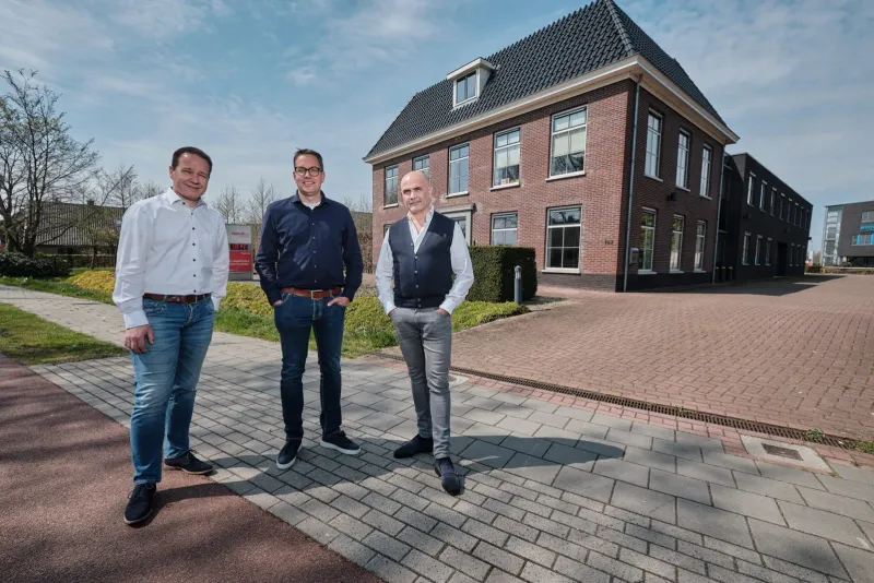 Drie mannen in zakelijke kleding voor een bakstenen kantoorpand op straat