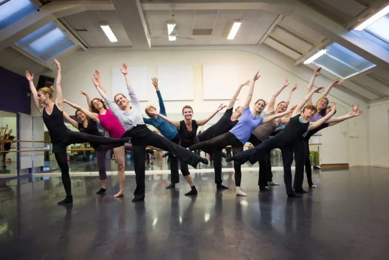 Dansgroep in een lichte studio maakt gelijktijdig een sprong met de armen omhoog