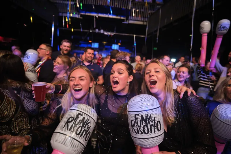 Feestend clubpubliek juicht met opblaasbare microfoons in een donkere zaal met podiumlichten