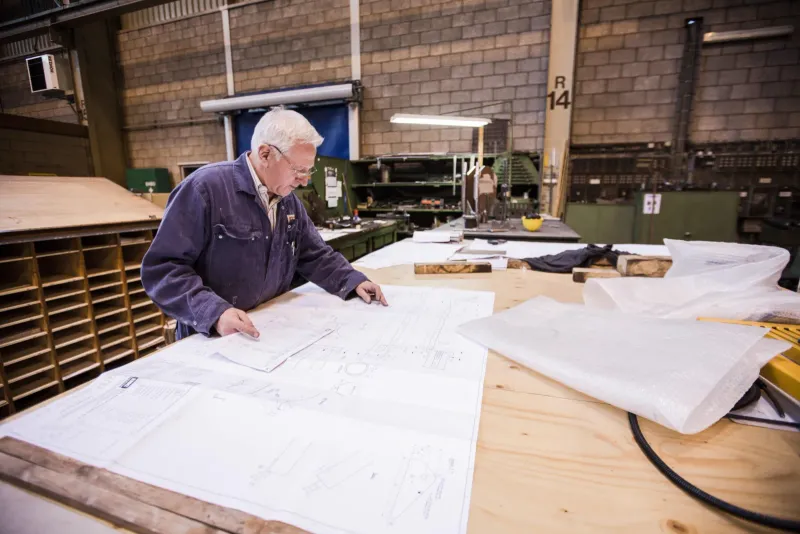 Oudere man bestudeert technische tekeningen op een grote tafel in een werkplaats