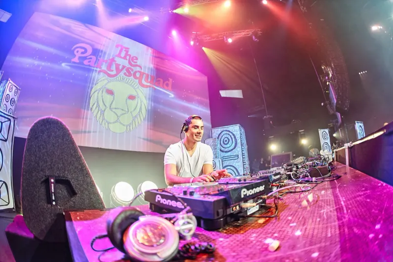 Dj achter draaitafels op een podium met een groot led-scherm en roze verlichting