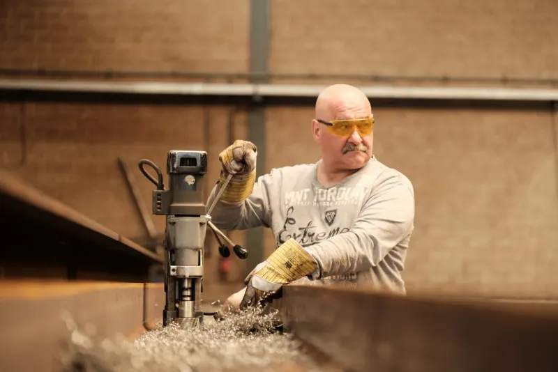 Man met veiligheidsbril bedient een kernboormachine terwijl het stof in het rond vliegt