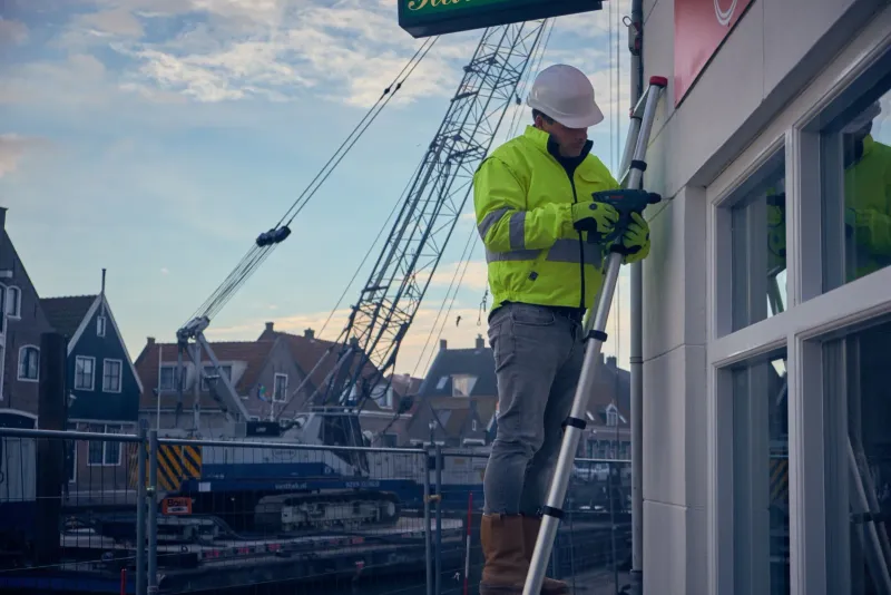 Werknemer in veiligheidskleding op een ladder controleert de ramen van een gebouw bij een haven