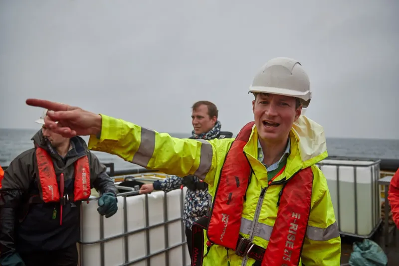 Twee mannen in veiligheidskleding en reddingsvest op het water, een van hen wijst iets aan
