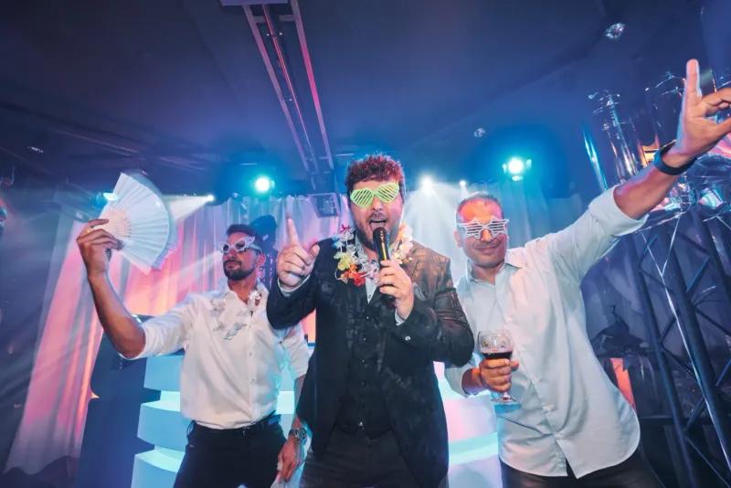 Drie feestende mannen met drankjes op een verlichte dansvloer met kleurrijke clubverlichting
