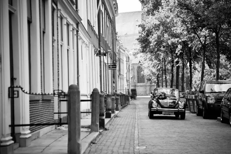 Zwart-witbeeld van een stille straat met een oldtimer en een kerktoren in de verte