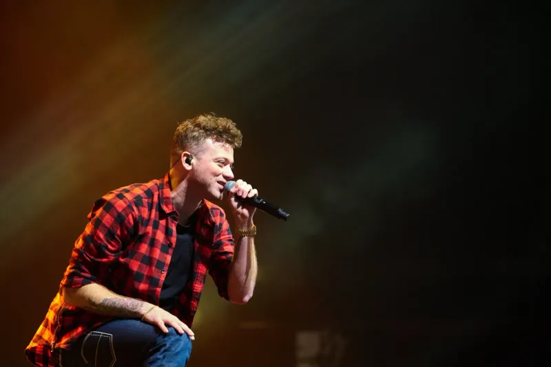 Zanger in een rood geruit overhemd treedt op met handmicrofoon in een warme spotlight