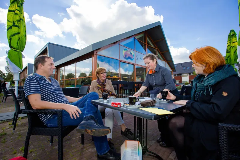 Vier mensen aan een buitentafel bij een modern houten paviljoen
