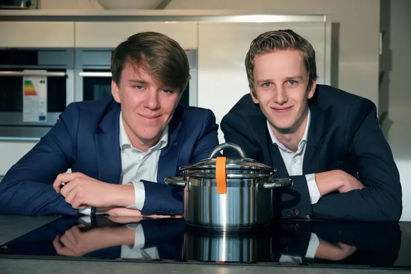Twee jonge ondernemers leunen op een tafel met een snelkookpan tussen hen in