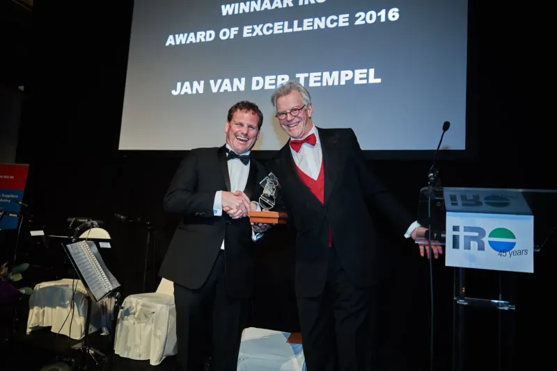 Man in smoking krijgt op een podium een award uitgereikt voor een groot projectiescherm