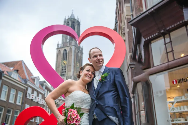 Bruidspaar poseert in een groot roze hartobject met de Domtoren op de achtergrond