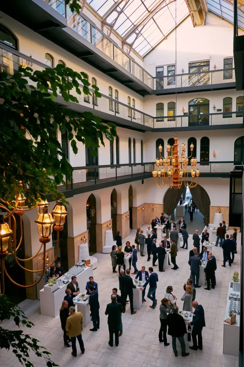 Netwerkreceptie in het glasoverkapte atrium van een historisch pand met gasten in pak aan statafels