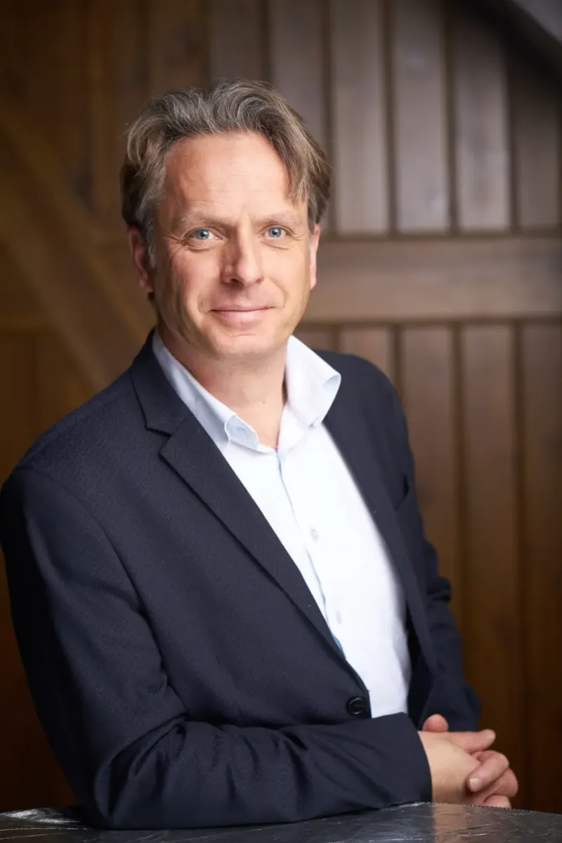 Zakelijk portret van een man in donker colbert tegen een houten wand