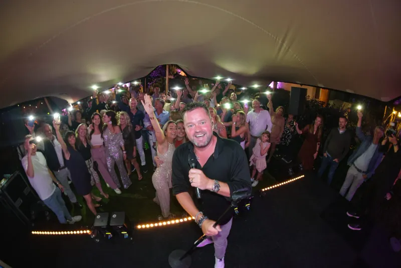 Feestende gasten onder een tent met lichtslingers terwijl een artiest met microfoon tussen het publiek staat