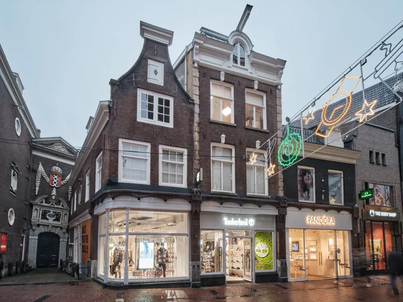 Historisch grachtenpand met trapgevel en verlichte winkelpui in de schemering